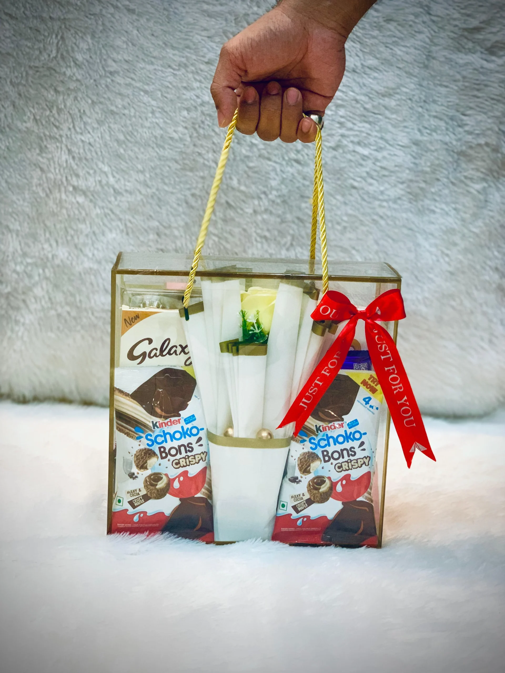 . A hand presents a bag of chocolates tied with a red ribbon, indicating a festive or special occasion.<br />
