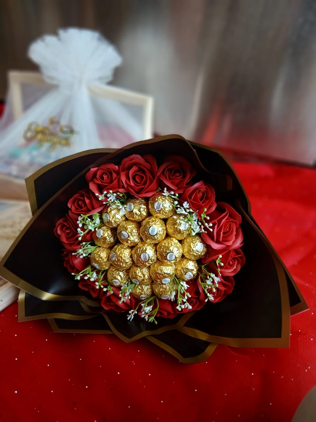  A bouquet of red roses alongside a box of chocolates on a vibrant red tablecloth.<br />
