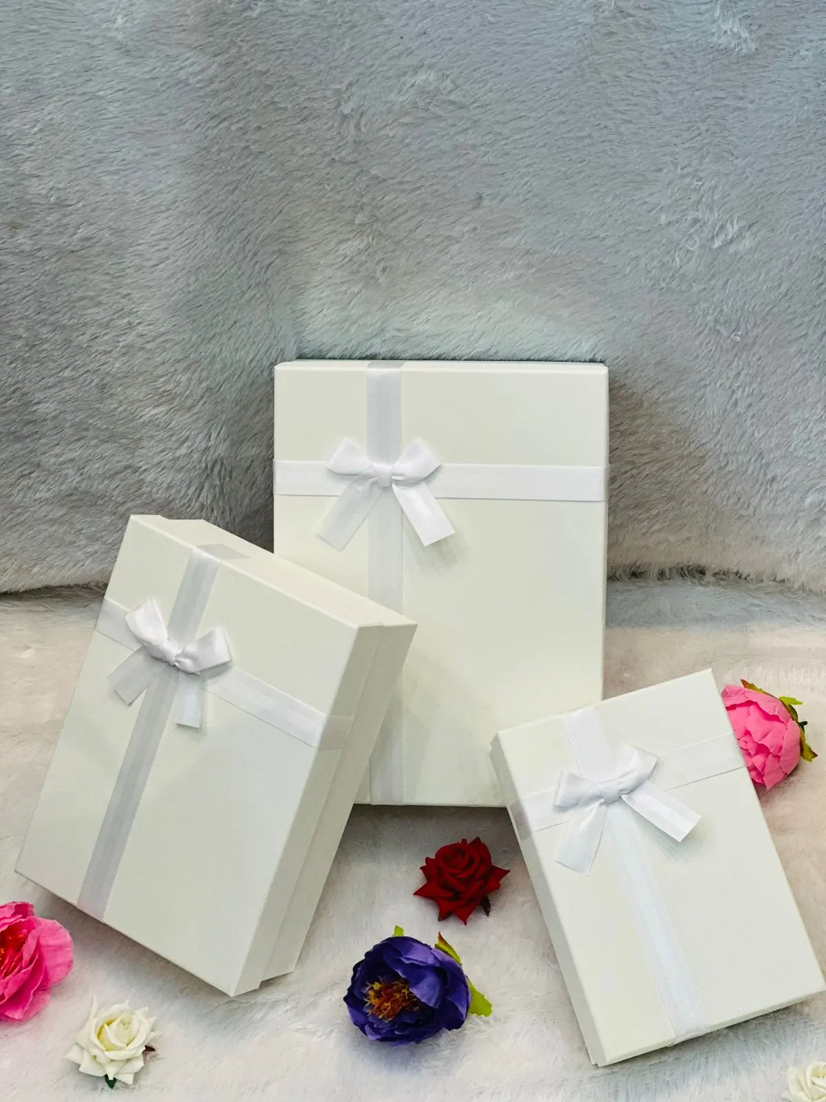 Three white gift boxes adorned with colorful ribbons and flowers, arranged neatly on a surface.